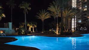 En pool som används för kvällsbad, med palmer och en byggnad i bakgrunden.