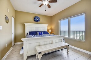 A bedroom with a bed, a ceiling fan, a window with a view, and a bench. - Shores of Panama 1804 (Panama City Beach)
