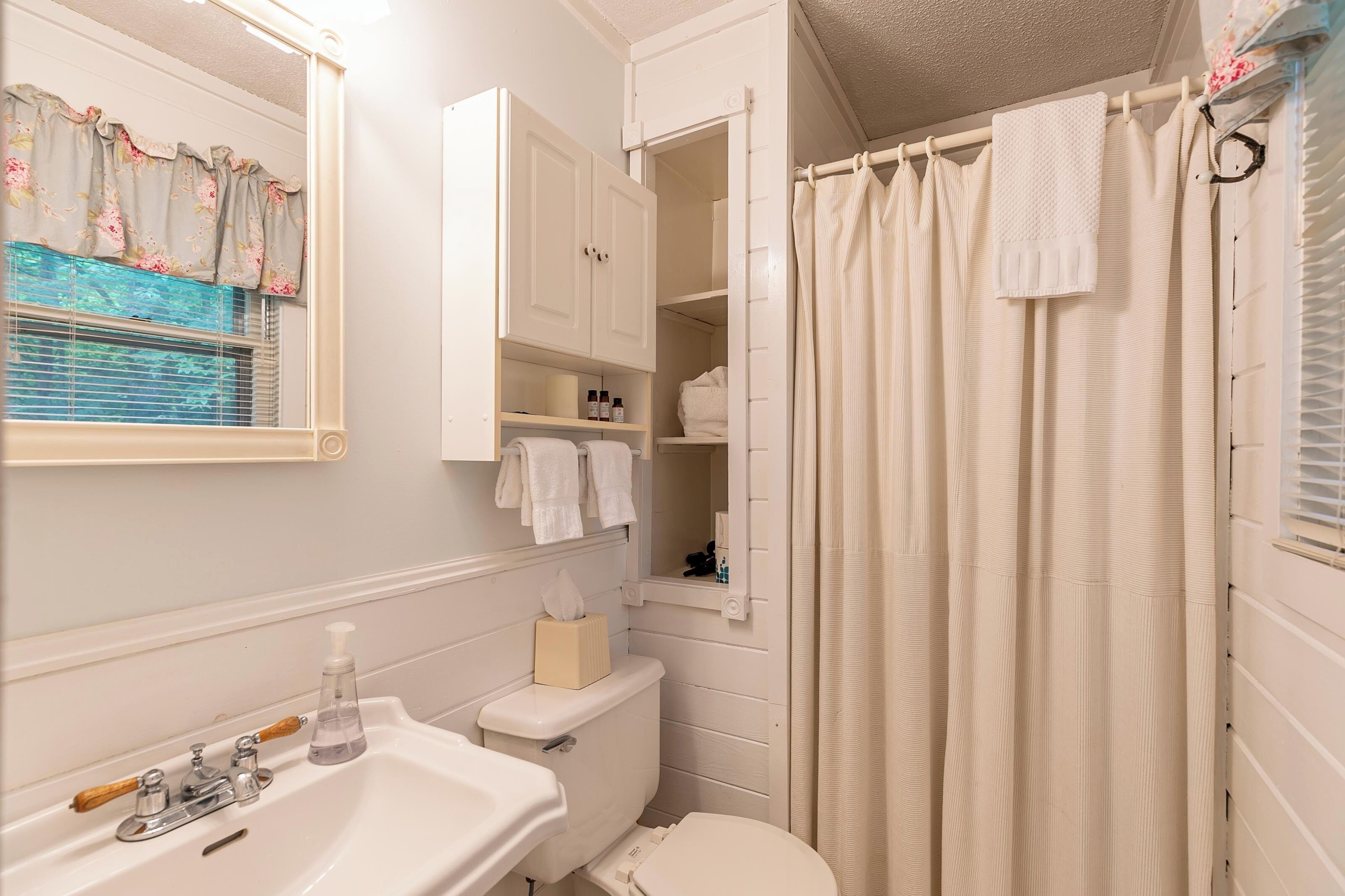 A bathroom with a sink, toilet, and open cabinet with toiletries.