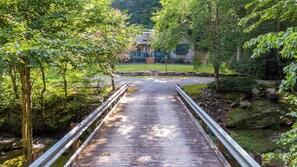 A wooden bridge leading to a house with a porch, surrounded by lush greenery. - Creek House (Boone)