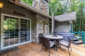 A stone exterior wall, a welcome sign, a glass door, wicker chairs, a round table, and a hot tub. - Creek House (Boone)