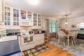 A kitchen with white cabinets, a stove, a sink, and a dining area with a table and chairs. - Creek House (Boone)