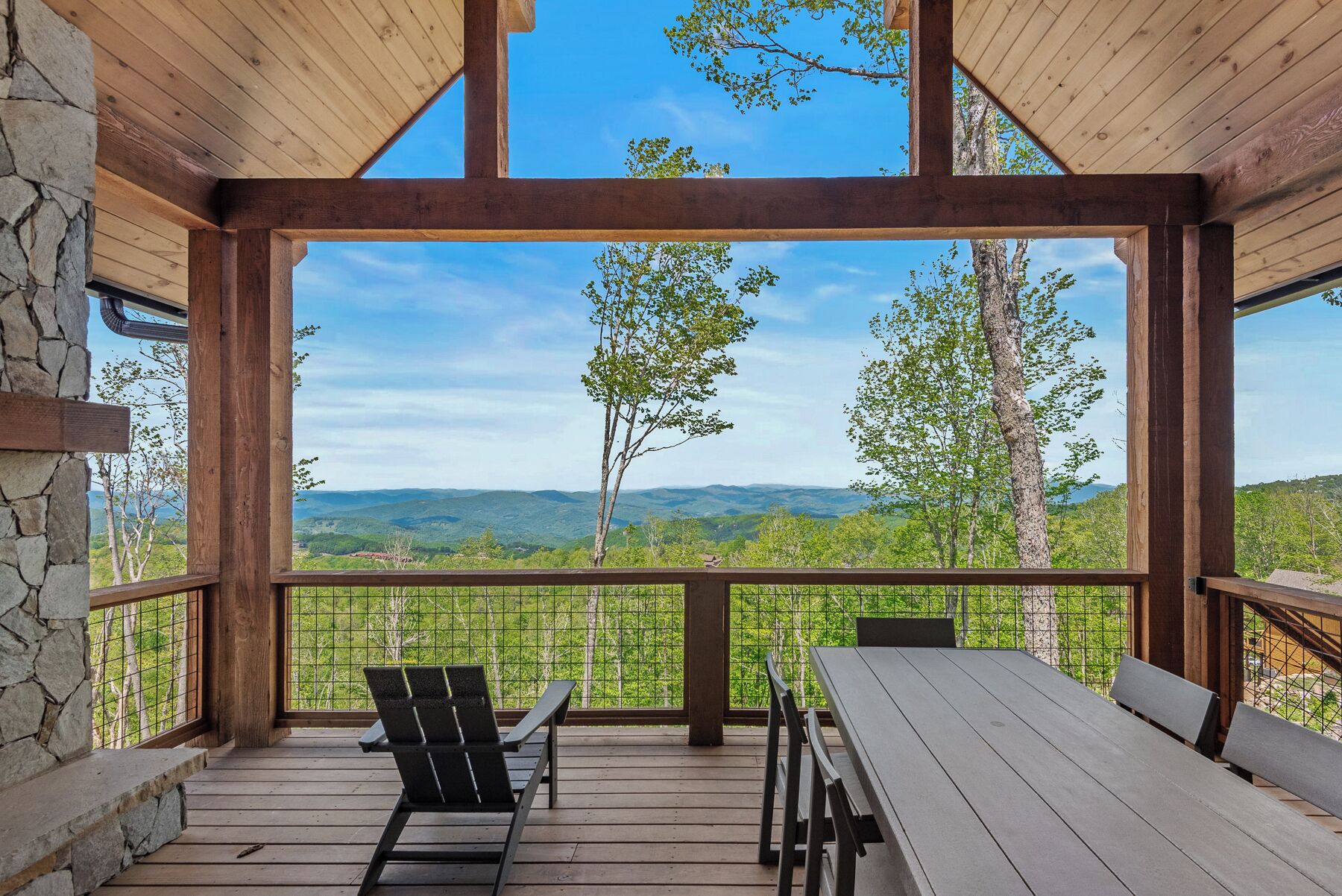 Eine Holzterrasse mit einer Steinsäule, einem Tisch und zwei Stühlen mit Blick auf eine Berglandschaft.