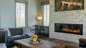 A living room with a stone fireplace, leather sofa, and a coffee table with a tray of items. - Zion at Eagles Nest (Banner Elk)