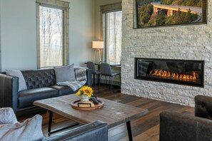 A living room with a stone fireplace, leather sofa, and a coffee table with a tray of items. - Zion at Eagles Nest (Banner Elk)