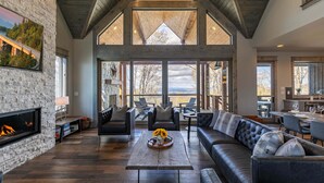 A spacious living room with a fireplace, leather sofas, a coffee table, and a large window overlooking a scenic view. - Zion at Eagles Nest (Banner Elk)