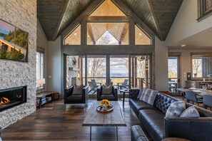 A spacious living room with a fireplace, leather sofas, a coffee table, and a large window overlooking a scenic view. - Zion at Eagles Nest (Banner Elk)