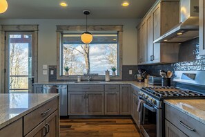 Une cuisine moderne avec des meubles en bois, une cuisinière en acier inoxydable et une grande fenêtre donnant sur les arbres.