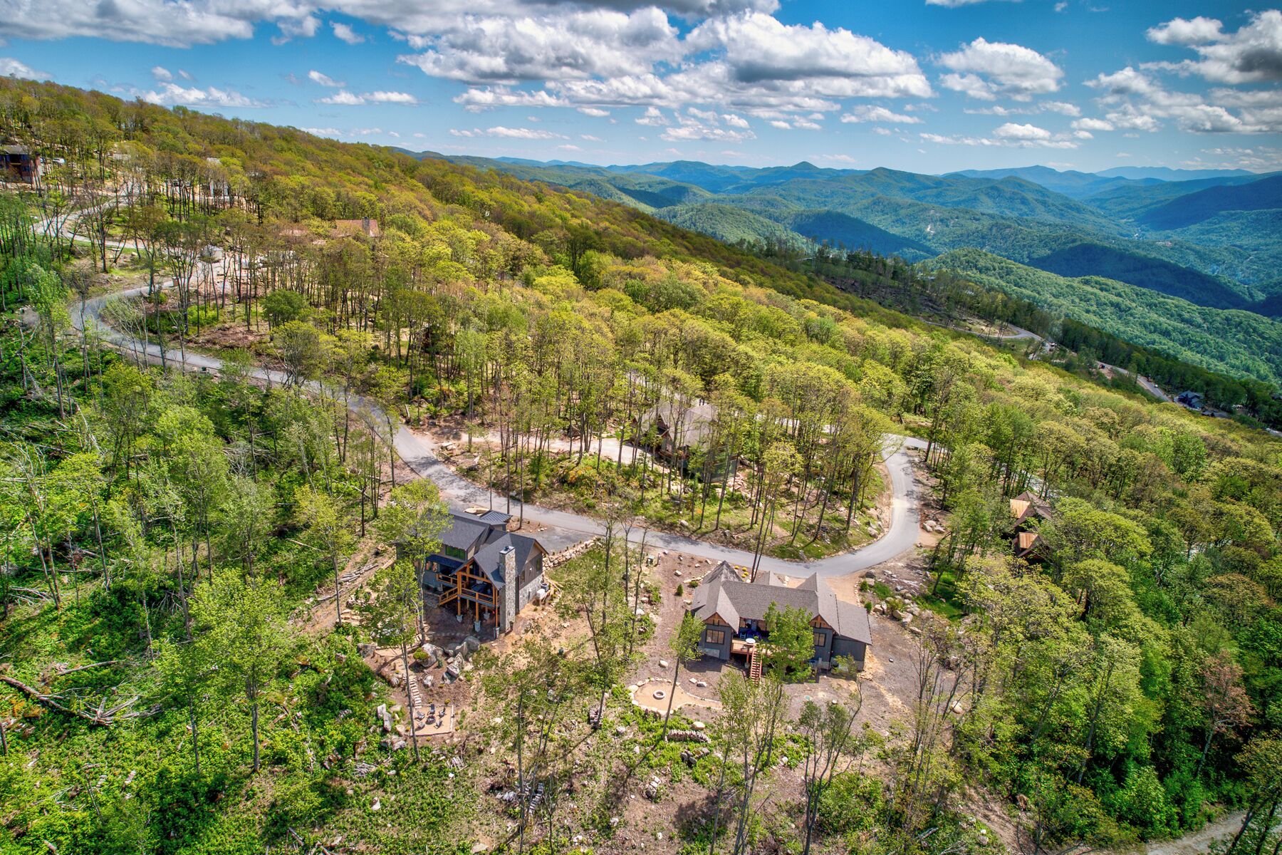 A remote cabin with a dirt road, surrounded by dense forest and mountains.