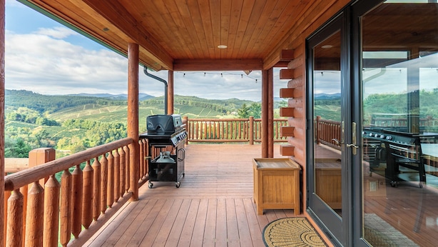 A wooden deck with a grill, a view of the countryside, and a glass door leading to an outdoor area. - Chasing Clouds Cabin (Fleetwood)
