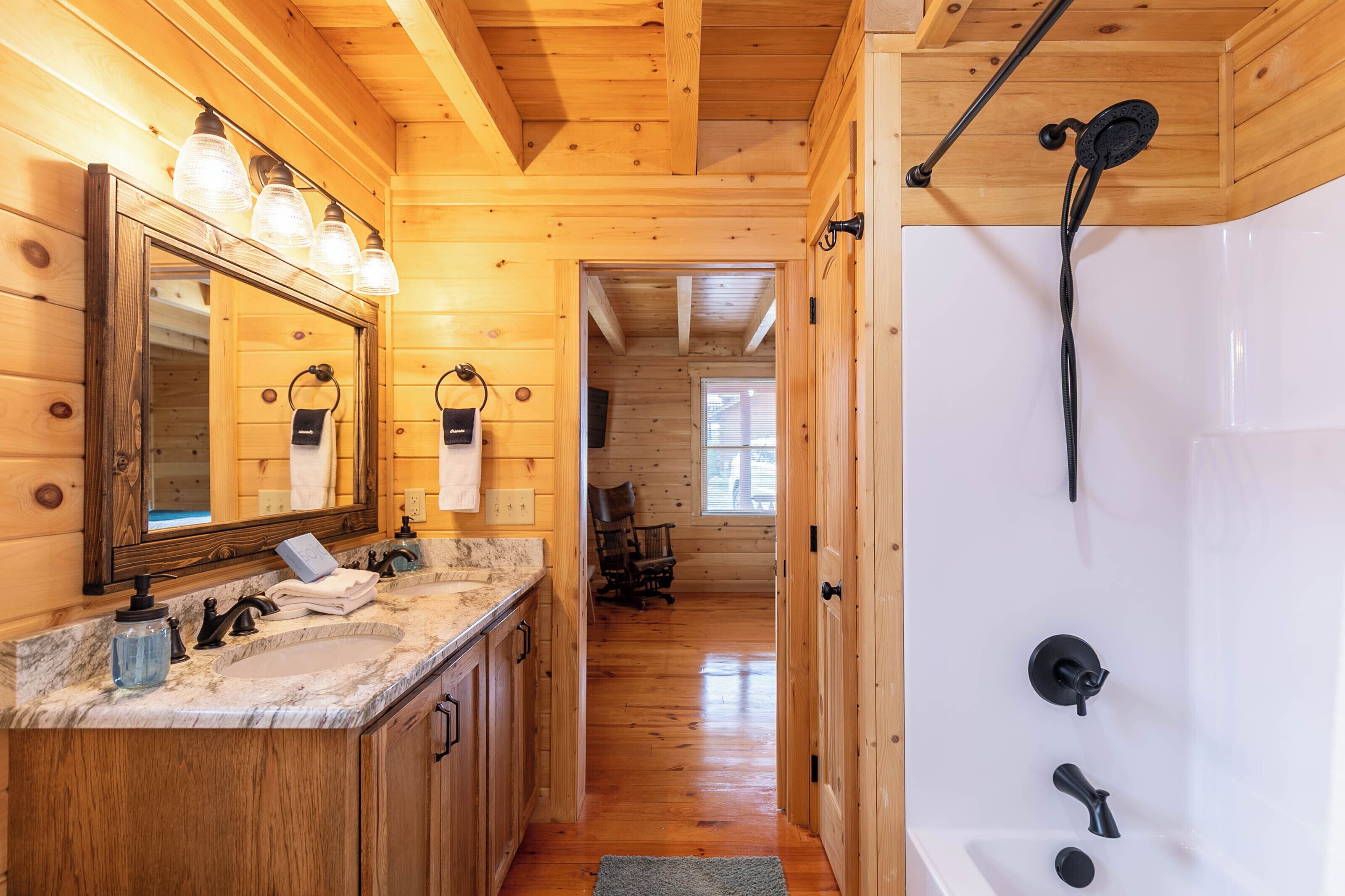 Interior de una cabaña de madera con un baño que incluye una bañera grande, un tocador con espejo y una ducha.