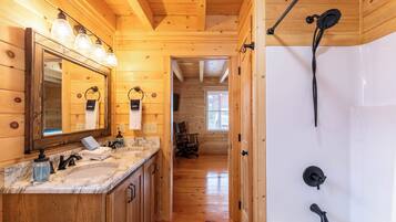 Interior de una cabaña de madera con un baño que incluye una bañera grande, un tocador con espejo y una ducha.