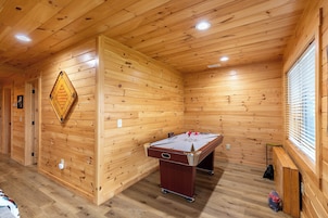 Una habitación con suelo de madera, mesa de billar y dardos.