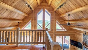 A wooden cabin interior with a high ceiling, large windows, and a balcony with a wooden railing. - Chasing Clouds Cabin (Fleetwood)