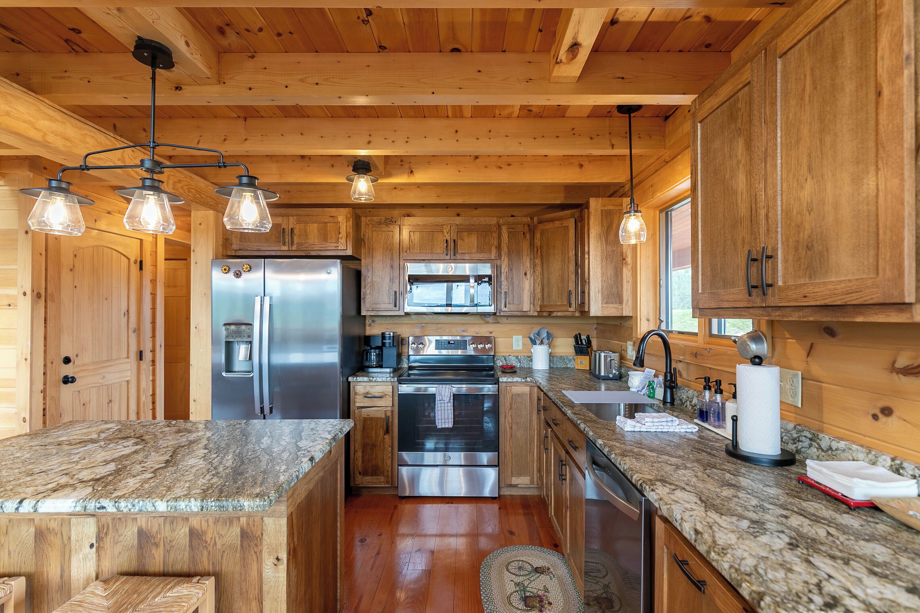 A wooden cabin interior with a kitchen featuring granite countertops, stainless steel appliances, and a central island.