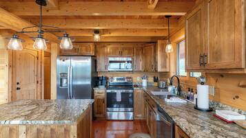 A wooden cabin interior with a kitchen featuring granite countertops, stainless steel appliances, and a central island.
