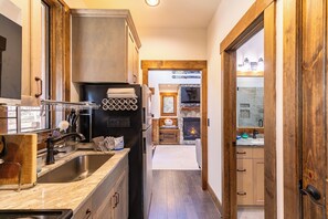 Eine Küche mit einem großen Spülbecken, einem Herd und einem Kühlschrank. Eine Holztür führt in einen anderen Raum.