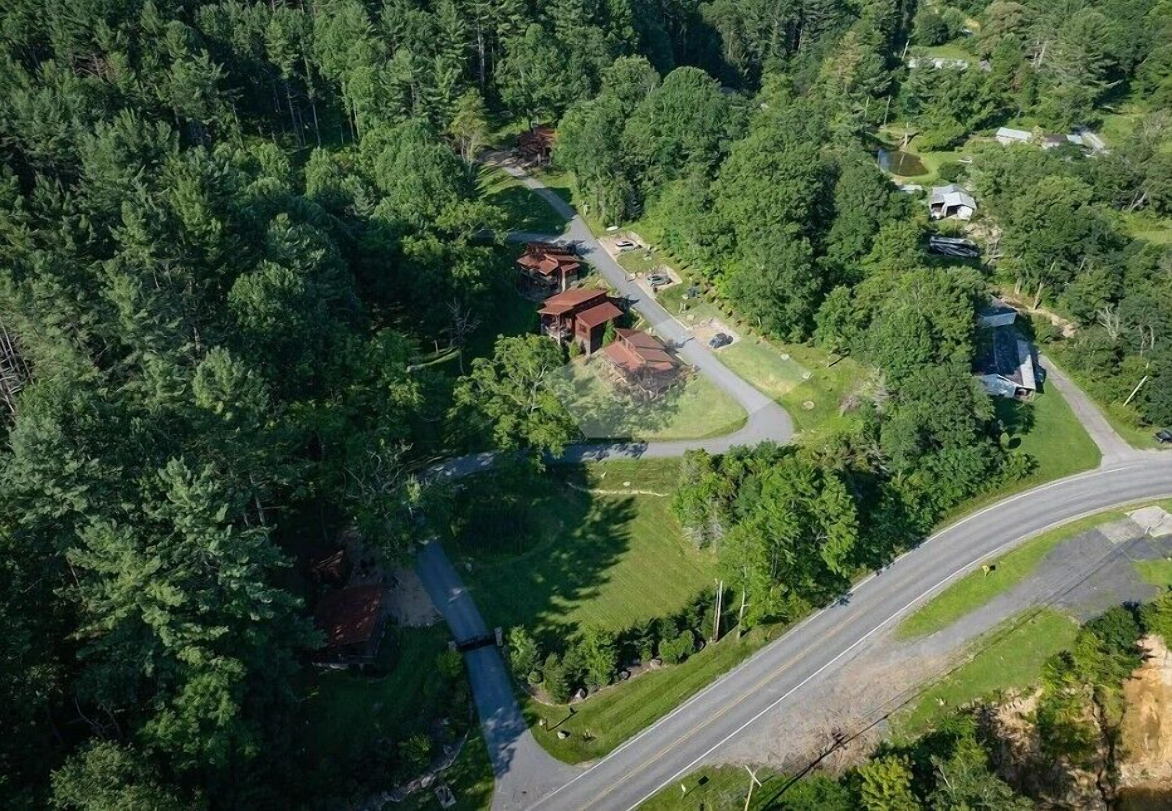 An aerial view of a forested area with a road, a small building, and a larger structure with a sloped roof.