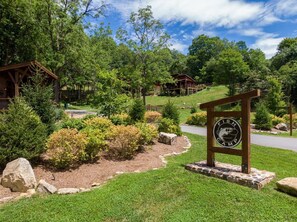A lodge with a wooden sign, surrounded by lush greenery and a stone pathway. - Ripple Run at Eagles Nest (Banner Elk)