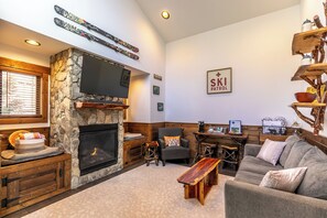 A cozy living room with a stone fireplace, a flat-screen TV mounted above it, and a ski-themed sign on the wall. - Ripple Run at Eagles Nest (Banner Elk)