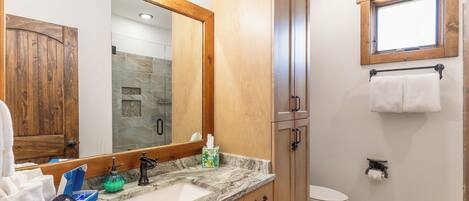 A bathroom with a wooden vanity, a large mirror, a marble countertop, a toilet, and a window.