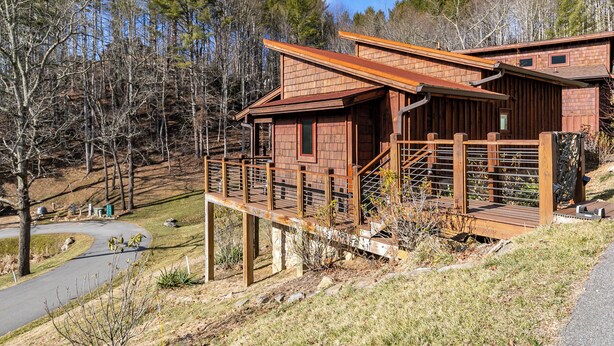 A wooden cabin with a deck, surrounded by trees. - Ripple Run at Eagles Nest (Banner Elk)