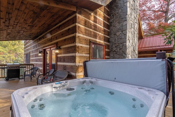 A wooden cabin with a hot tub, outdoor seating, and a stone wall. - River Ridge (Boone)