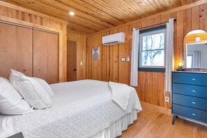 Une pièce aux murs lambrissés, avec un lit, une commode et une fenêtre.