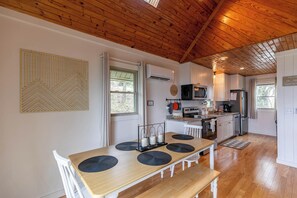 Een moderne keuken met witte kasten, een houten plafond en een eethoek met een houten tafel en stoelen.