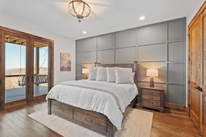 A bedroom with a large bed, two bedside tables, a wooden door, and a view of the outdoors. - Altitude Adjustment at Eagles Nest (Elk Park)