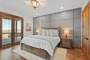 A bedroom with a large bed, two bedside tables, a wooden door, and a view of the outdoors.