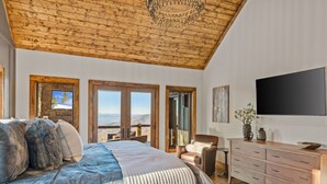 A bedroom with a large bed, a wooden ceiling, a TV, and a view through the window. - Altitude Adjustment at Eagles Nest (Elk Park)