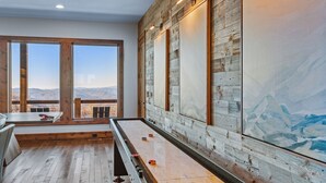A room with a shuffleboard table, wooden walls, and a large window with a mountain view. - Altitude Adjustment at Eagles Nest (Elk Park)