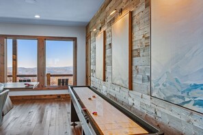 Ein Zimmer mit Shuffleboard-Tisch, Holzwänden und einem großen Fenster mit Bergblick.