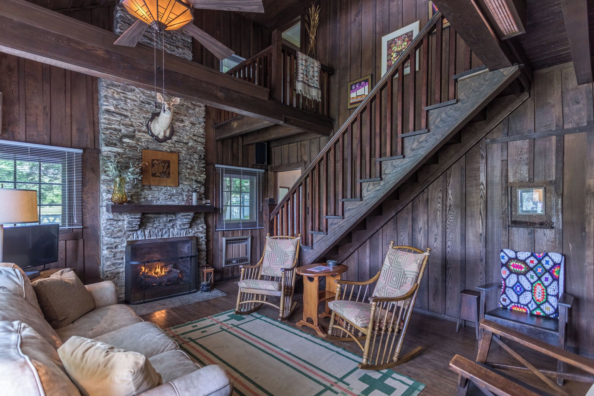 A rustic interior with a stone fireplace, wooden staircase, and a cozy seating area.