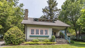 A two-story house with a porch, surrounded by lush greenery and trees. - The Suddreth Cottage (Blowing Rock)
