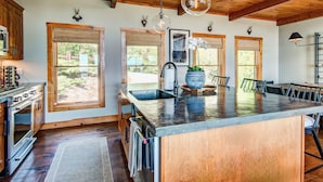 A modern kitchen with large windows, wooden cabinets, and a central island. - Owls Nest (Blowing Rock)