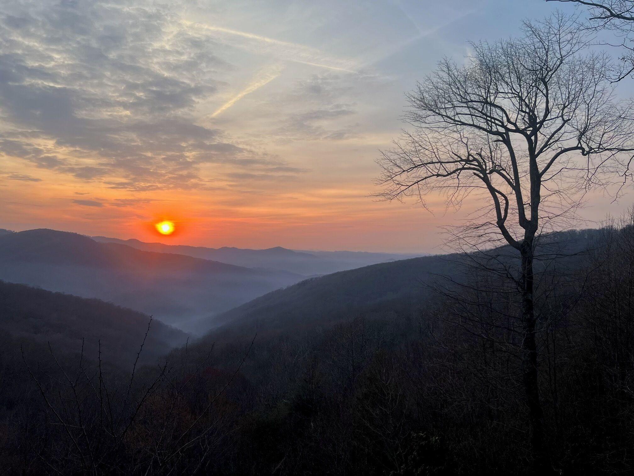 A mountain landscape with a clear sky and a sun setting or rising behind the hills.