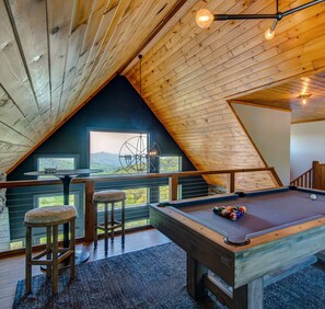 A cozy room with a pool table, a bar area, and a view of the outdoors.