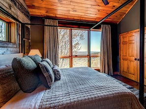 Un dormitorio con una cama grande, una ventana con cortinas y techo de madera.