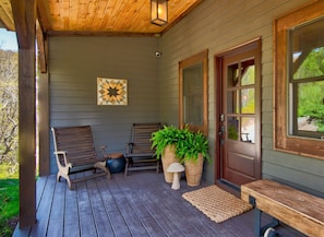 A wooden porch with two benches, a potted plant, and a door with a window.