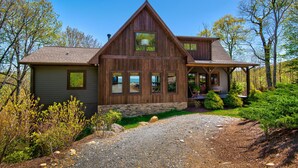 A wooden cabin with a stone foundation, large windows, and a porch. - Owls Nest (Blowing Rock)