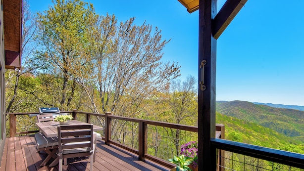 A wooden deck with a table and chairs, overlooking a mountainous landscape. - Owls Nest (Blowing Rock)