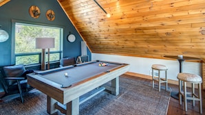A cozy room with a pool table, wooden ceiling, and a window overlooking greenery. - Owls Nest (Blowing Rock)