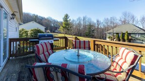 A deck with a glass table and striped chairs, a grill, and a view of a forested area. - Petes Alpine Retreat (Banner Elk)