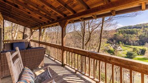A wooden deck with wicker furniture and a view of a valley. - Daniel Boone Lodge (Boone)