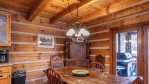 A wooden cabin interior with a dining table, chairs, a coffee machine, and a large wooden cabinet. - Daniel Boone Lodge (Boone)