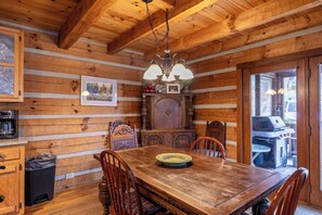 Ein Holzblockhaus-Innenraum mit Esstisch, Stühlen, einer Kaffeemaschine und einem großen Holzschrank.