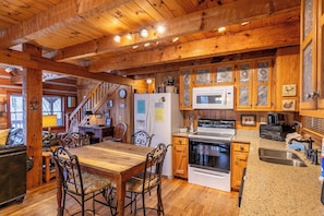 Interior rústico de una cabaña con una mesa de comedor de madera, sillas, una cocina con estufa, microondas y armarios.