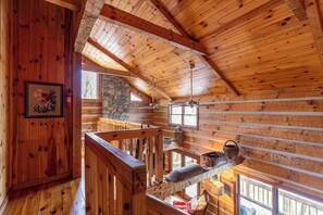 A wooden cabin interior with a loft bedroom, stone wall, wooden beams, and a fireplace. - Daniel Boone Lodge (Boone)